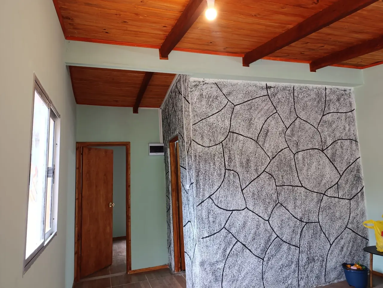 Sala terminada con cielorraso de madera, pared decorada en piedra y puerta al dormitorio