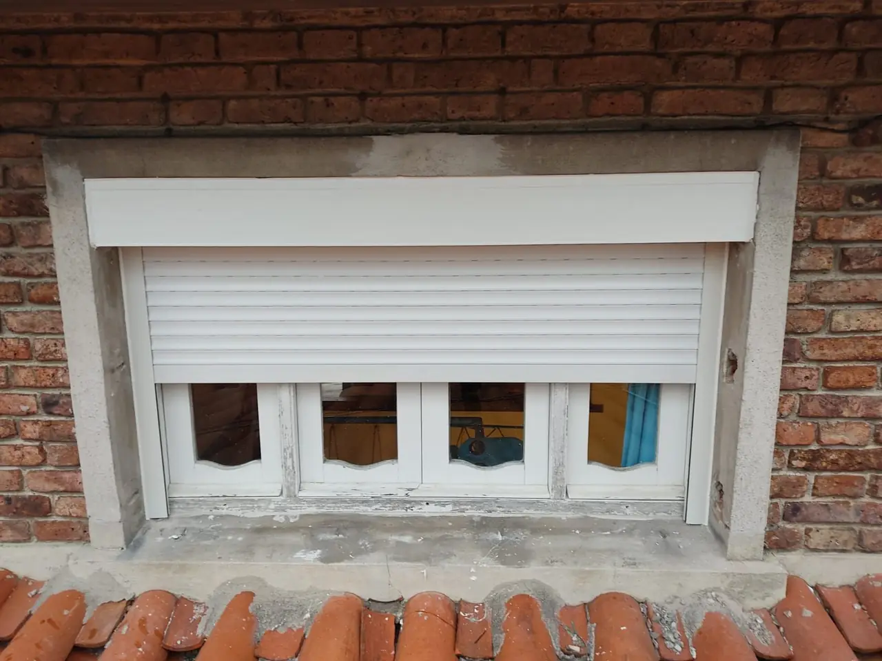 Cortinas de enrollar de PVC blanco en una ventana de ladrillo visto