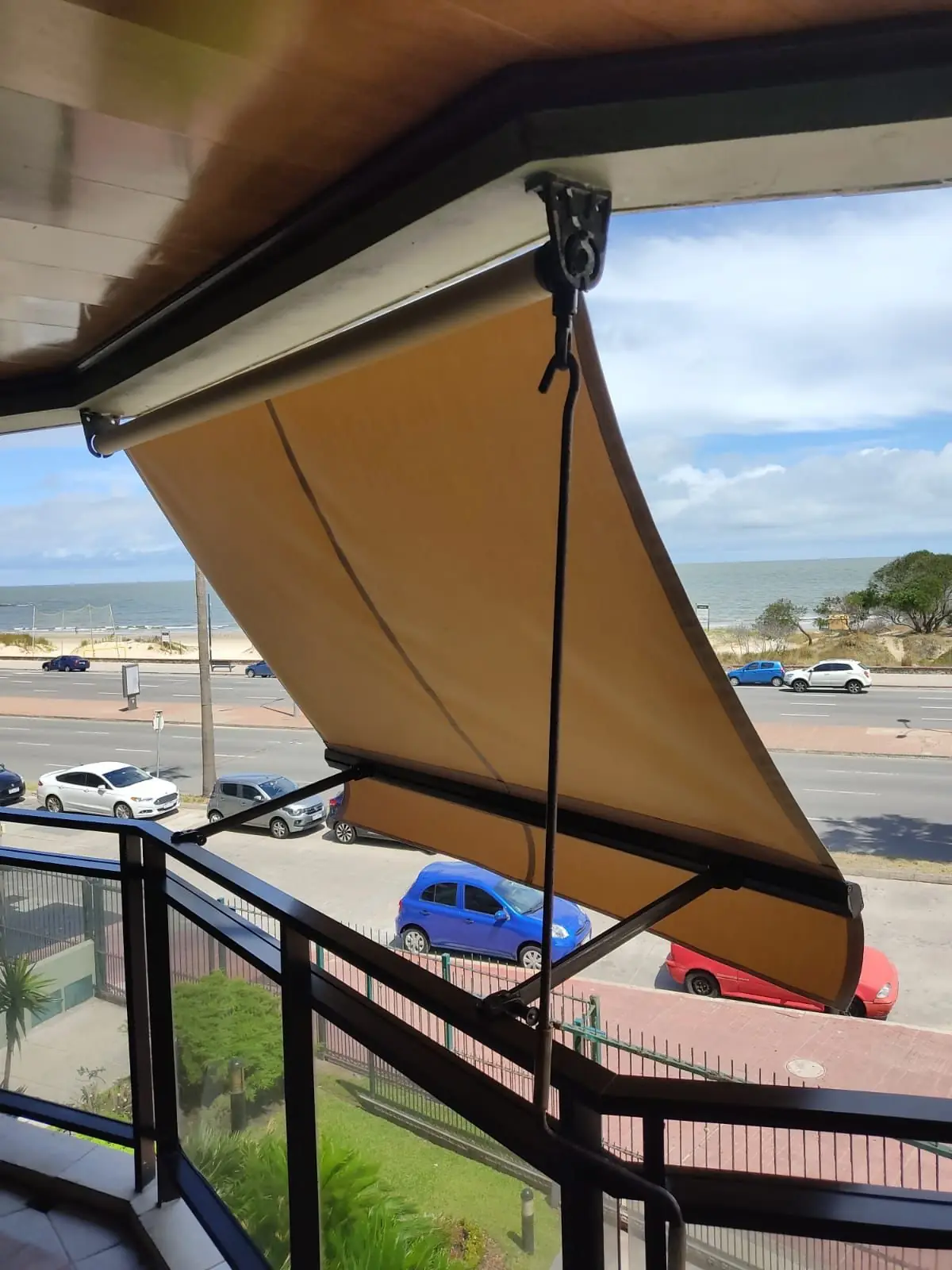 Toldo de brazo invisible extendido sobre un balcón frente a la playa